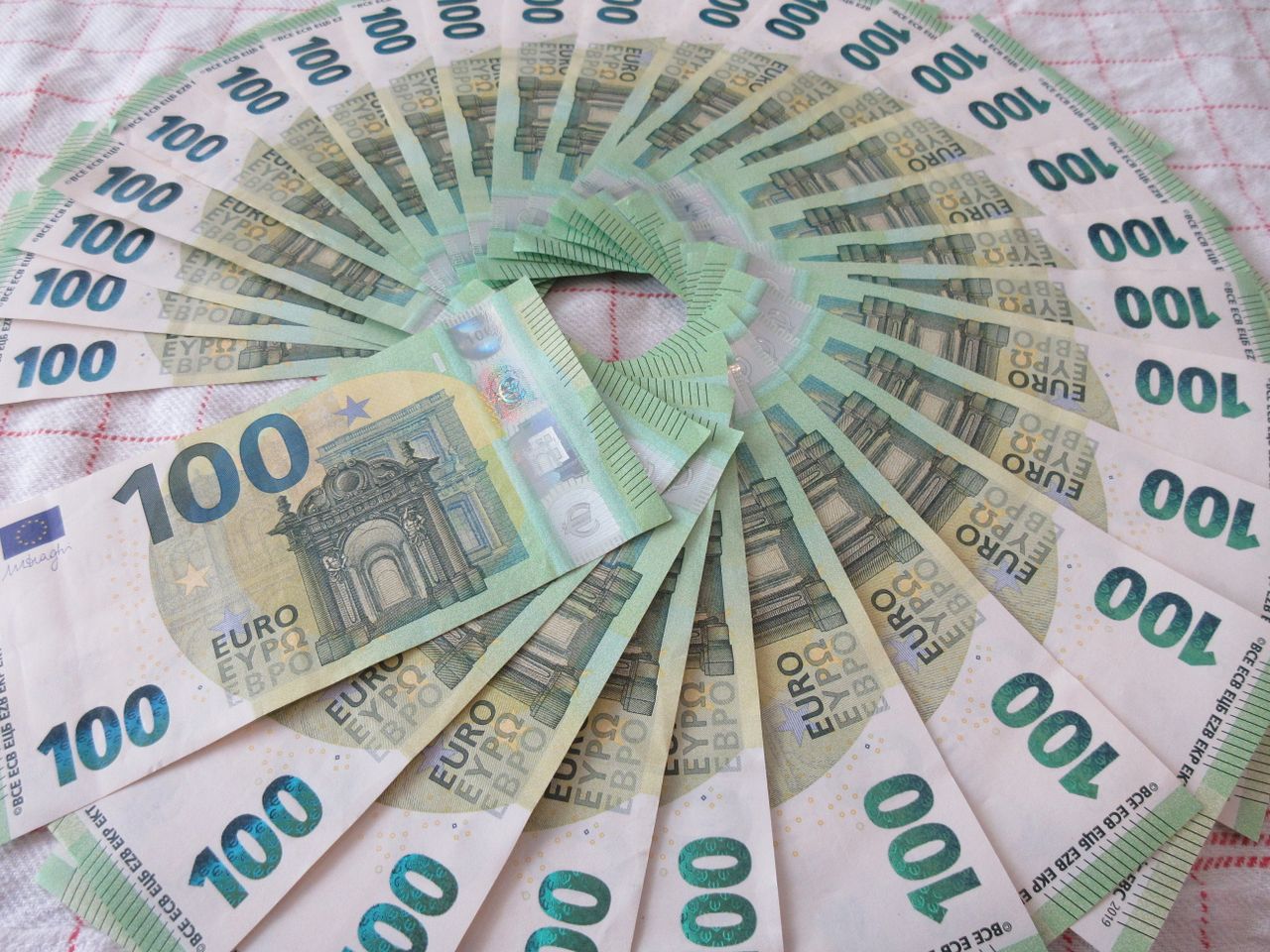 Home Close-up of a fan of 100 euro banknotes arranged in an artistic circle pattern on a textile surface.