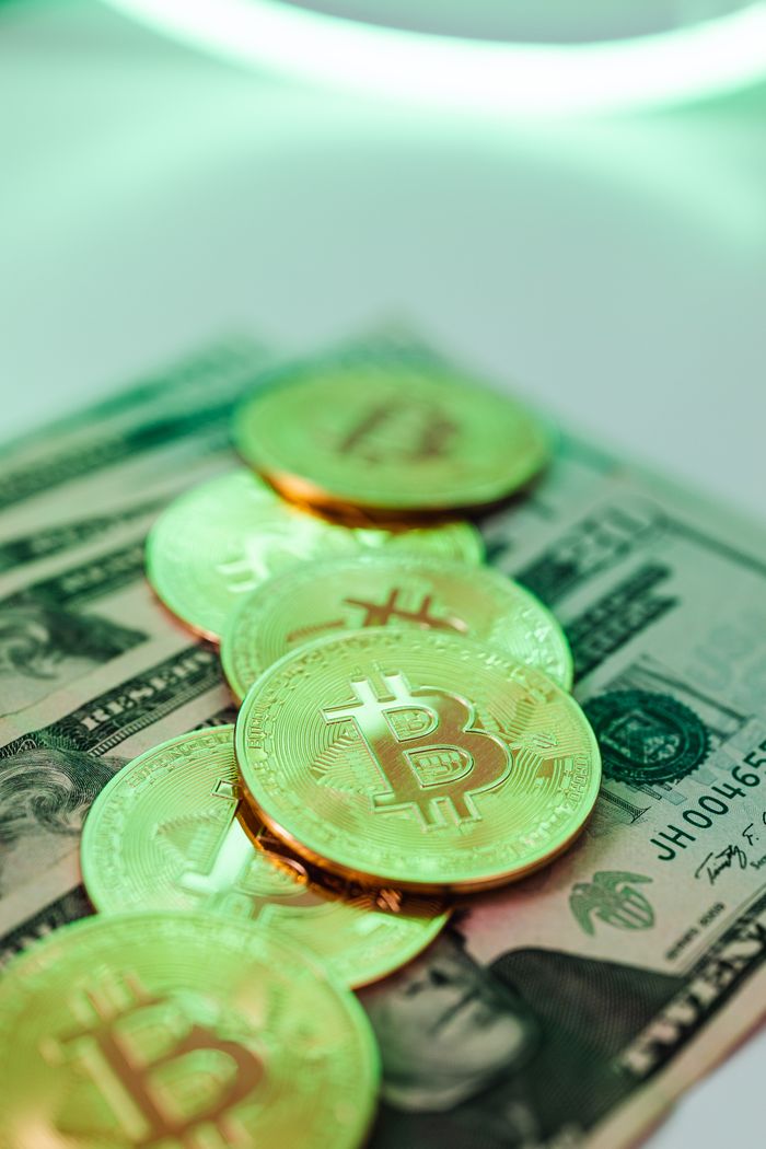 gallery-04 Golden Bitcoin coins placed over American dollar banknotes, highlighting crypto and cash economy.