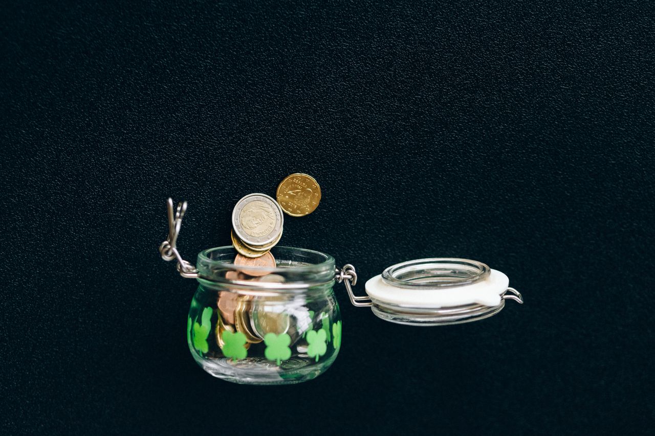 Home Glass jar with coins falling into it on a black background, symbolizing savings.